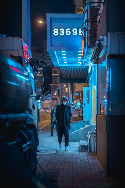 穿着黑夹克的男人在夜间走在人行道上